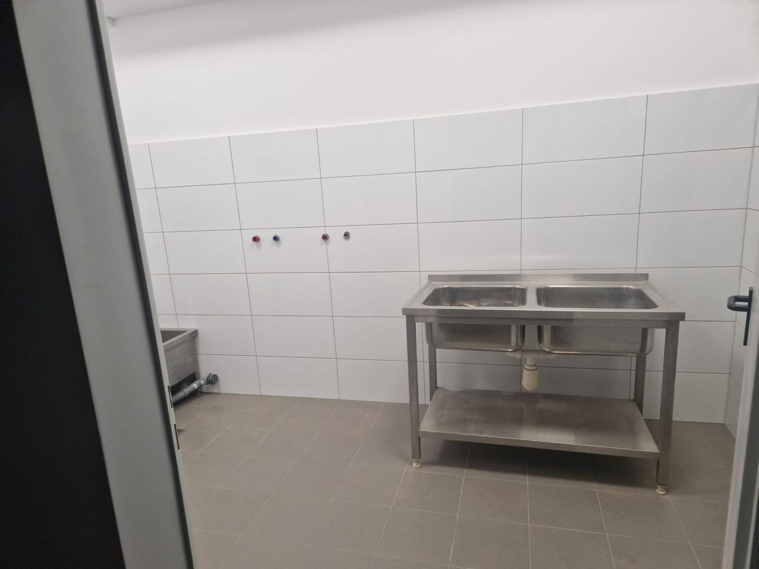Stalowy zlew dwukomorowy przy białych płytkach i szarej posadzce